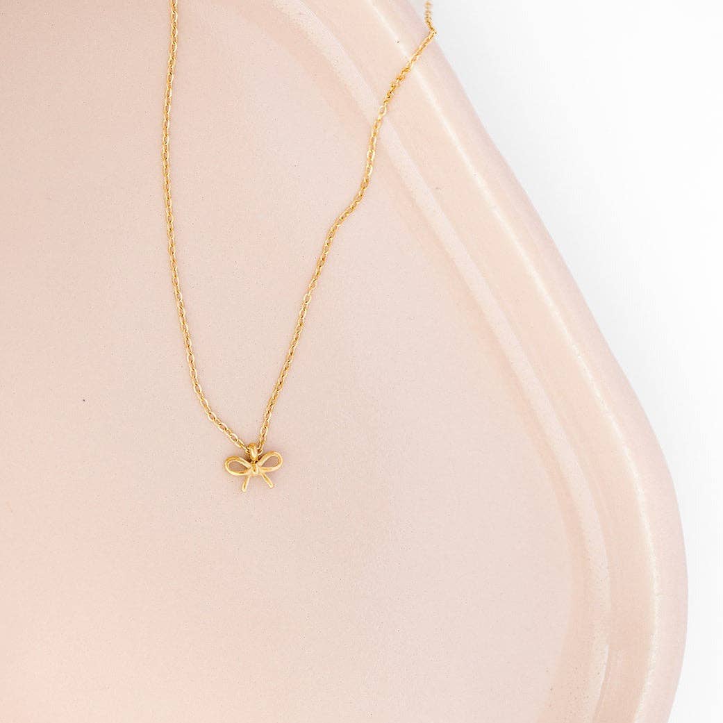 Gold bow pendant necklace from Pip Pop Post, stylish accessories featuring a delicate bow charm on a chain.