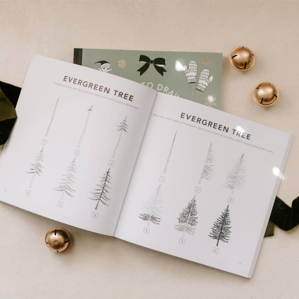 Book open to pages with evergreen tree illustrations on a beige surface with decorative items.