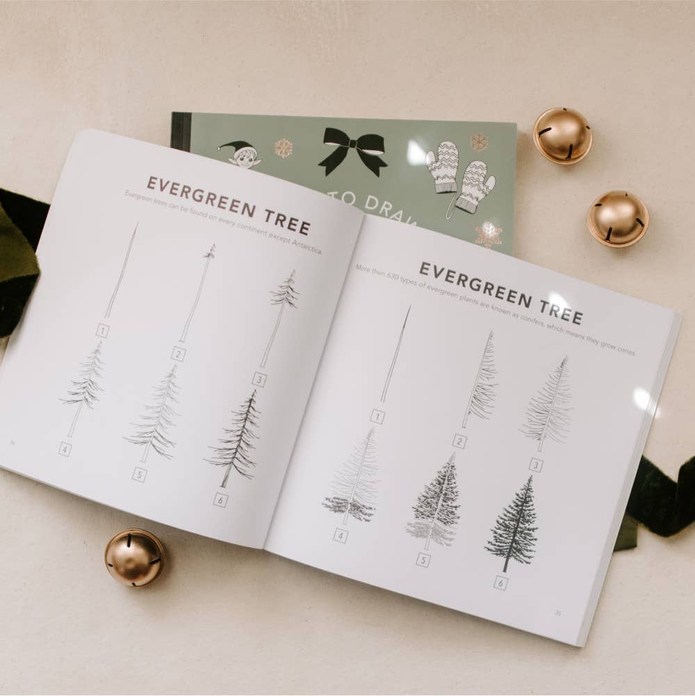 Book open to pages with evergreen tree illustrations on a beige surface with decorative items.